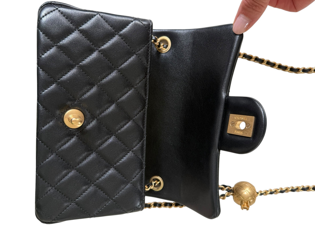 Chanel Pearl Crush Mini Flap Bag ist aus schwarzem Lammleder und zeichnet sich durch goldene Hardware sowie eine verstellbare Kette mit einer ikonischen Perlenkugel aus.
